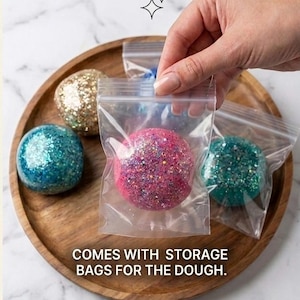 May include: Several spherical balls of glittery dough in various colours including pink, blue, gold, and teal. Each ball is individually packaged in a clear plastic resealable storage bag. The text on the image reads, COMES WITH STORAGE BAGS FOR THE DOUGH.