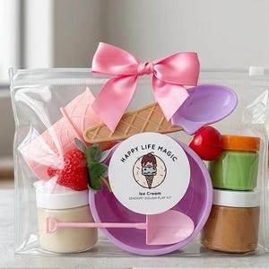 May include: A clear plastic bag filled with an ice cream sensory dough play kit. The kit includes a pink bow, play dough, a purple bowl and spoon, a strawberry, and other accessories. The kit is labeled "Happy Life Magic".