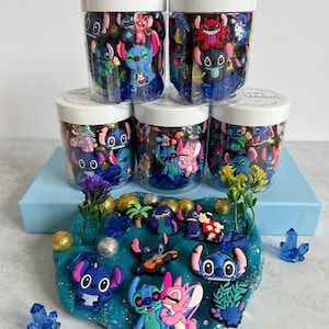 Pode incluir: Kits sensoriais com berloques do personagem Stitch. Potes de plástico transparente contêm berloques temáticos do Stitch, e uma base de jogo azul apresenta berloques, cristais e decorações adicionais. O texto "HAPPY LIFE MAGIC SENSORY KITS" é visível.