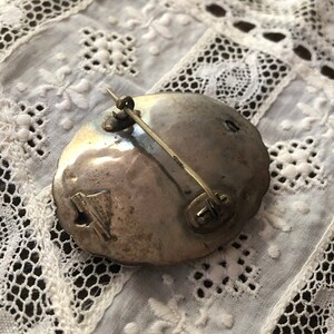 May include: Silver-toned brooch with a decorative design. The brooch has a pin and catch closure on the back.