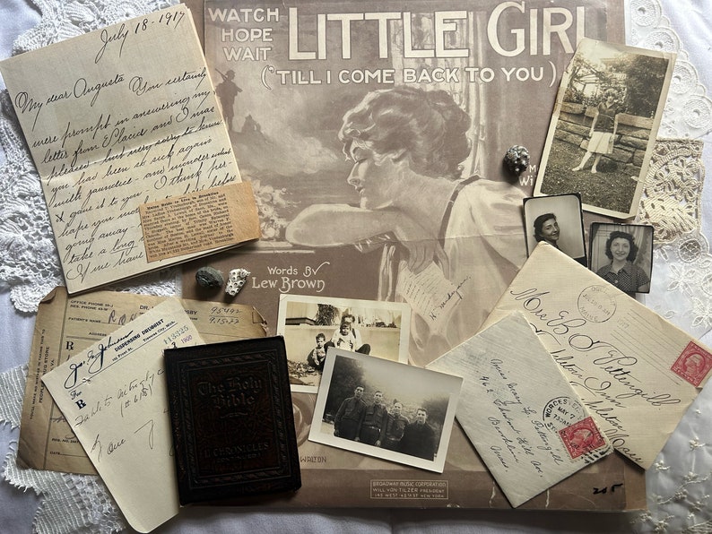 Puede incluir: Una colecci&oacute;n de ef&iacute;meras vintage que incluye una portada de partitura para la canci&oacute;n "Little Girl (Till I Come Back To You)", una carta manuscrita fechada el 18 de julio de 1917, un peque&ntilde;o libro encuadernado en cuero titulado "The Holy Bible" y varios sobres con sellos.
