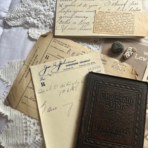 Puede incluir: Un libro antiguo encuadernado en cuero marr&oacute;n con el t&iacute;tulo "The Holy Bible" y "II Chronicles (Continued)" en relieve en la portada. El libro est&aacute; sobre una superficie blanca con un trozo de papel y una receta manuscrita.