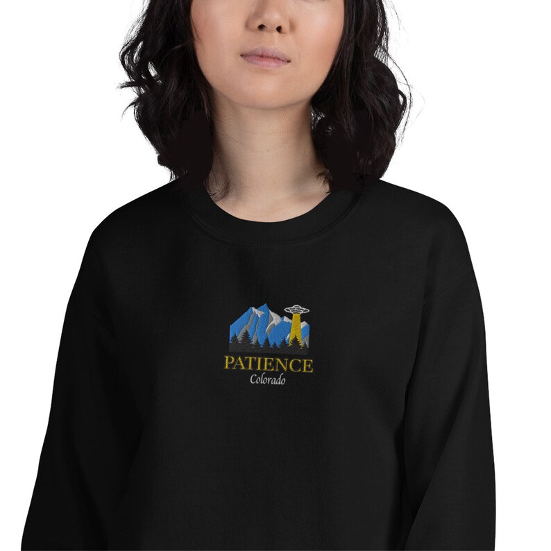 May include: Black sweatshirt with a graphic of a mountain range and a UFO with the text "Patience Colorado" in gold.
