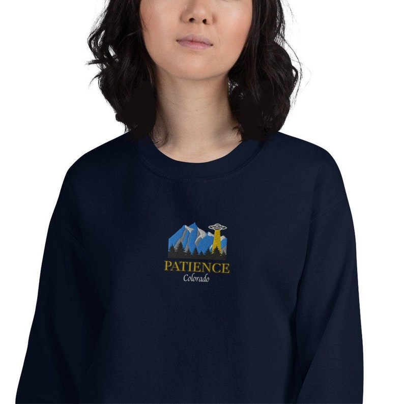 May include: A navy blue sweatshirt with a graphic of a mountain range and a UFO. The text "PATIENCE Colorado" is printed below the graphic.