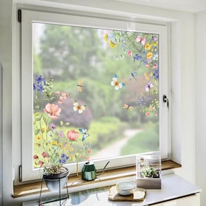 May include: A window with a floral and butterfly design. The window features a frosted glass effect with colorful illustrations of flowers, butterflies, and dragonflies. The window is set in a white frame, with a view of a blurred green background.