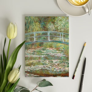 May include: A painting of a green bridge over a pond with water lilies. The bridge has a white railing and is surrounded by green trees and foliage. The water is a light blue color and the lilies are white and pink.