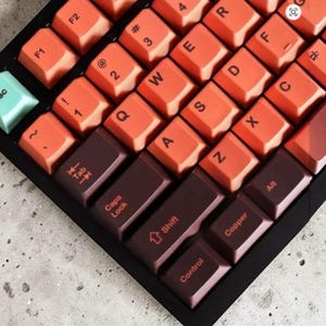 May include: Close-up of a mechanical keyboard with orange and brown keycaps. The keyboard has a black frame and features keys with letters, numbers, and symbols. The Esc key is a light teal color.