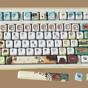 Op de afbeelding: Een aangepast mechanisch toetsenbord met een cr&egrave;mekleurig frame en keycaps met verschillende illustraties. De keycaps hebben een mix van kleuren, waaronder blauw, groen en bruin, met de cijfers en letters in wit. Het toetsenbord bevat een bijpassende polssteun.
