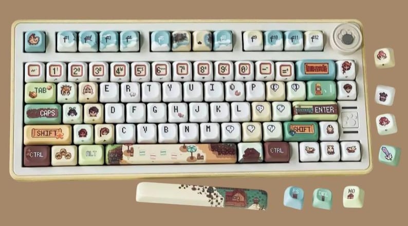 Op de afbeelding: Een aangepast mechanisch toetsenbord met een cr&egrave;mekleurig frame en keycaps met verschillende illustraties. De keycaps hebben een mix van kleuren, waaronder blauw, groen en bruin, met de cijfers en letters in wit. Het toetsenbord bevat een bijpassende polssteun.