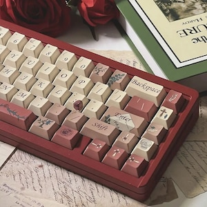 May include: A custom mechanical keyboard with a burgundy case and off-white keycaps. The keycaps feature decorative floral and botanical designs, with a rose and tree motif. The keyboard has a vintage aesthetic, with a classic font.