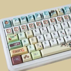 Op de afbeelding: Een witte mechanische toetsenbord met aangepaste keycaps. De keycaps tonen verschillende illustraties en tekst, waaronder cijfers, symbolen en woorden als "TAB", "CAPS", "SHIFT" en "CTRL". De keycaps hebben een pastel kleurenschema met diverse ontwerpen.