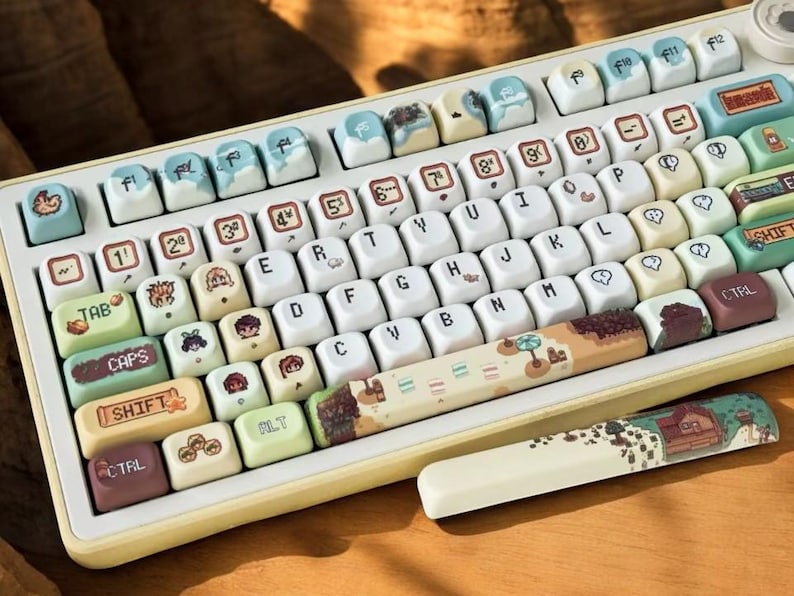 Op de afbeelding: Een aangepast mechanisch toetsenbord met cr&egrave;mekleurige toetsen en een gele lijst. De keycaps hebben unieke illustraties en ontwerpen, waaronder landschappen en karakterkunst. Het toetsenbord bevat een bijpassende polssteun.