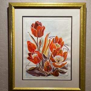 Op de afbeelding: Een ingelijste print van fel oranje tulpen met bruine en groene stelen. Het kunstwerk staat tegen een lichte achtergrond en is ingelijst in een goudkleurige lijst. De print is gesigneerd en genummerd.