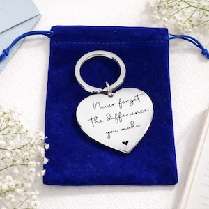 May include: A silver heart-shaped keyring with the inscription "Never forget the difference you make" and a small black heart. The keyring is on a blue velvet pouch.