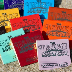 May include: A collection of colorful matchboxes with the text "THE INCENSE MATCH" in a stylized font. The boxes are in various colors, including blue, red, orange, and pink. The bottom of one box reads "goddess of egypt".