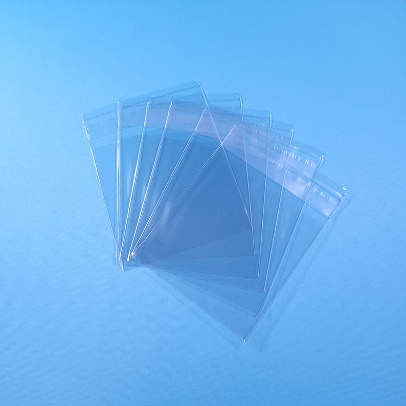 May include: A stack of clear plastic sleeves, probably for protecting cards or other items, against a light blue background.