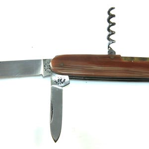 May include: A brown handled pocket knife with a corkscrew, a large blade, and a smaller blade. The knife has a decorative design on the handle.