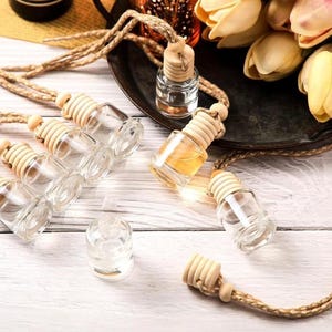 May include: Clear glass car air freshener bottles with wooden caps and brown rope hangers. Some bottles are filled with a yellow liquid. The bottles are arranged on a white wooden surface.