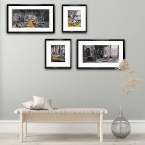 May include: Four black framed pictures on a light grey wall above a white wooden bench. The pictures are all in black and white except for one which has a pink orb in the centre.