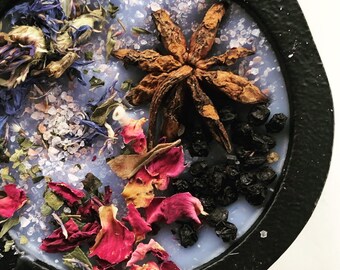 May include: A close-up of a purple candle with dried flowers, star anise, and black berries embedded in the wax.