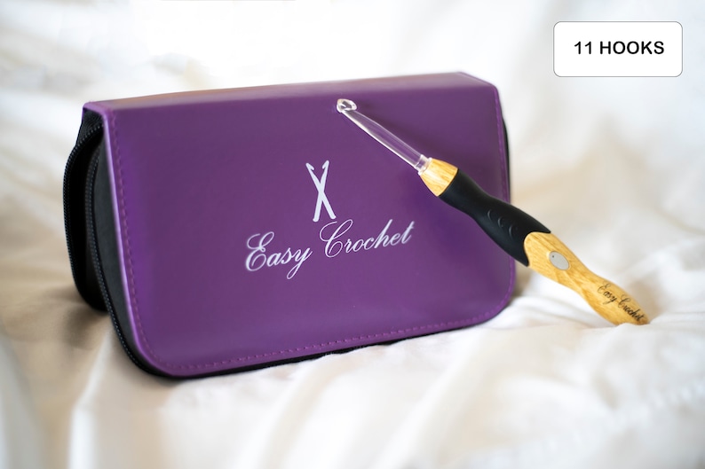 May include: A purple crochet hook case with the text "Easy Crochet" and a white X on the front. A single crochet hook with a wooden handle is lying next to the case. The case has a zipper closure. The text "11 HOOKS" is on a white rectangle in the upper right corner of the image.
