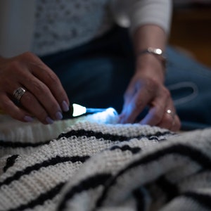 May include: A person is knitting a white and black striped crocheted blanket with a lighted needle.