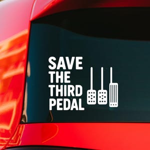 May include: A white vinyl car decal featuring the text "SAVE THE THIRD PEDAL" in a bold, sans-serif font, accompanied by a graphic illustration of three car pedals, including two perforated pedals and one accelerator pedal, applied to a window.
