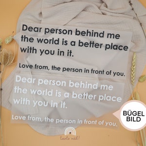 Könnte beinhalten: Eine weiße Karte mit dem Text "Dear person behind me the world is a better place with you in it. Love from, the person in front of you." zweimal wiederholt. Die Karte liegt auf einem beigefarbenen Hintergrund mit getrockneten Blumen.