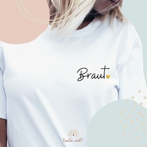 Könnte beinhalten: Weißes T-Shirt mit dem Wort "Braut" in schwarzer Schrift und einem kleinen goldenen Herzen.