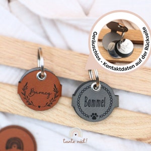 Könnte beinhalten: Zwei Leder-Hundemarken mit den eingravierten Namen "Barney" und "Bommel". Die Marken sind braun und grau mit dekorativen Designs. Die Marken sind an Schlüsselringen befestigt.