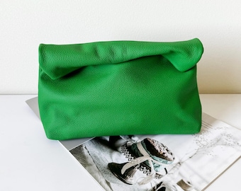 May include: A bright green leather clutch bag with a folded top. The bag is rectangular and sits on a magazine with a white background. The leather has a textured appearance.