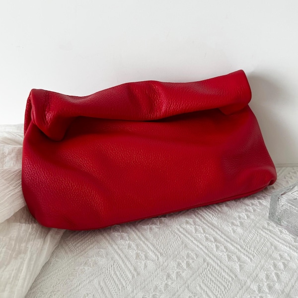 May include: A vibrant red clutch bag with a soft, pebbled texture and a folded top closure. The bag features a rectangular shape with rounded corners and a flexible, slouchy construction, showcasing a consistent deep red color throughout the exterior.