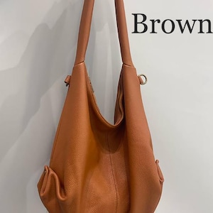 May include: A brown hobo bag with a textured surface, featuring a single long shoulder strap, a central vertical seam, and side pockets with metallic hardware. The word Brown is printed in black text on the upper right side of the image.
