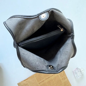 Puede incluir: Bolso tote de cuero negro con un bolsillo con cremallera en el interior. El bolso tiene un cierre de metal dorado.