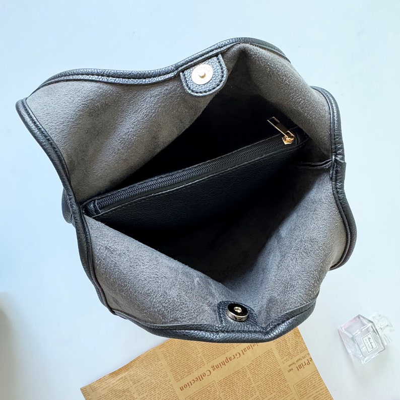 Puede incluir: Bolso tote de cuero negro con un bolsillo con cremallera en el interior. El bolso tiene un cierre de metal dorado.