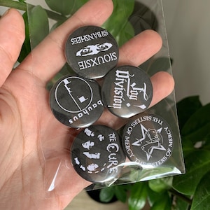 Può includere: Cinque badge a bottone neri e bianchi con i nomi delle band "Siouxsie and the Banshees", "Joy Division", "Bauhaus", "The Cure" e "The Sisters of Mercy".