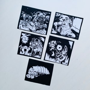 Può includere: Cinque illustrazioni in bianco e nero stampate su cartoncino bianco. Le illustrazioni presentano varie creature con un tema horror. Il testo "Mama I'm Scared" è incluso in una delle illustrazioni.