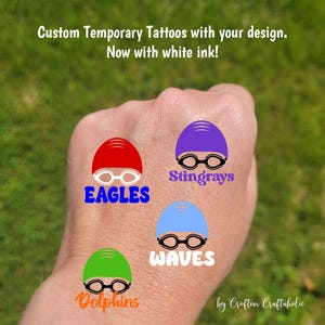 May include: Custom temporary tattoos with white ink, featuring designs of swim caps and goggles. The designs include the words "EAGLES", "Stingrays", "WAVES", and "Dolphins". The tattoos are in red, purple, blue, and green.