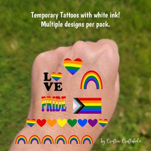 May include: Temporary tattoos with white ink featuring multiple designs per pack. Designs include rainbow hearts, rainbows, the word "LOVE", the word "PRIDE", and a rainbow flag with a progressive pride flag.