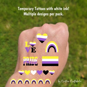 May include: Temporary tattoos with white ink featuring multiple designs per pack. Designs include hearts, rainbows, and the word "PRIDE" in a colorful font. The tattoos also feature the non-binary flag colors.