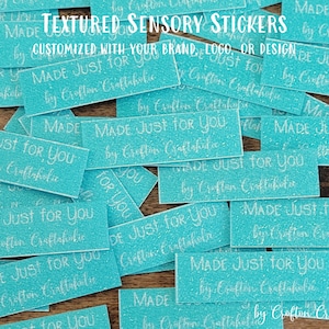 May include: A close-up of a pile of turquoise blue textured sensory stickers with the text "MADE JUST FOR YOU by Craftin' Craftaholic" printed in white on each sticker.