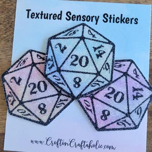 May include: Three iridescent glitter textured D20 dice stickers with black outlines. The dice are stacked on top of each other. The stickers are labeled with the numbers 2, 8, 14, and 20. The text "Textured Sensory Stickers" is at the top of the image. The text "www.CroftonCraftaholic.com" is at the bottom of the image.