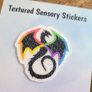 May include: A rainbow textured sensory sticker featuring a black dragon with wings. The sticker has a textured, sparkly finish.