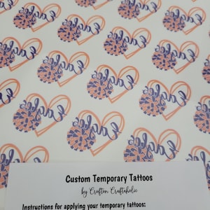 May include: A sheet of temporary tattoos with a heart design and the word "Eagles" in purple script. The heart is outlined in orange and filled with a purple and orange pom-pom. The text "Custom Temporary Tattoos by Crofton Craftaholic" is at the bottom of the sheet. Instructions for applying the tattoos are also included.