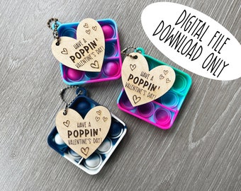 Puede incluir: Tres etiquetas de madera en forma de corazón con el texto "Have a Poppin' Valentine's Day!" unidas a juguetes pop-it coloridos.