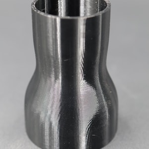 May include: A black plastic reducer fitting for connecting pipes or hoses of different diameters.