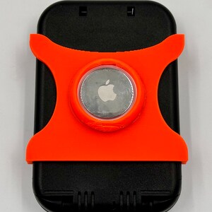 May include: A black phone case with an orange, 3D printed, rotating ring holder. The ring holder has a silver Apple logo in the center.