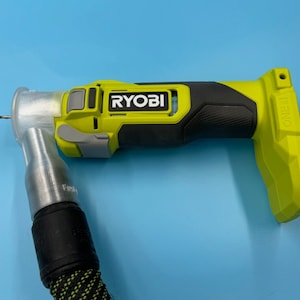 Könnte beinhalten: Ein gelber und schwarzer Ryobi Rechtwinkeldrill mit einem silbernen Aufsatz und einem schwarzen und grünen Kabel.