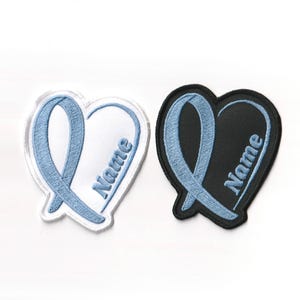May include: Two heart-shaped patches. One is white with a light blue ribbon design and the word "Name". The other is black with a light blue ribbon design and the word "Name".