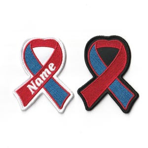 May include: Two embroidered iron-on patches in the shape of a red, white, and blue ribbon. The ribbon on the left has the word "Name" embroidered on it. The ribbon on the right is on a black background.